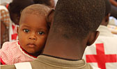 Foto: ein haitianisches Baby schaut über die Schulter eines Rotkreuzhelfers